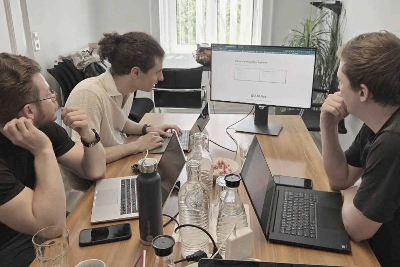 Drei Workshop-Teilnehmer mit Laptops an einem Tisch, im Hintergrund eine Folie zum EU AI Act